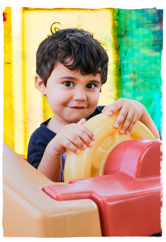 A little boy looking at the camera and holding a wheel on a play set.