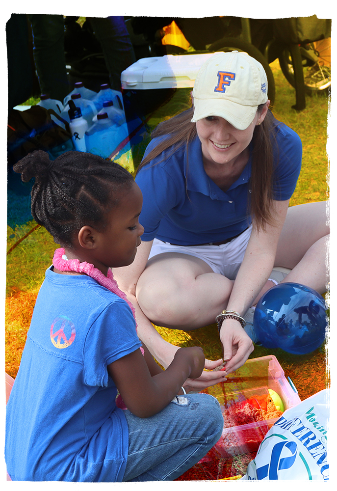 A woman speaking to a young girl while sitting on the ground.