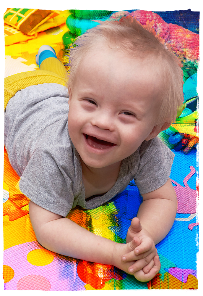 A young boy laying on a colorful mat.